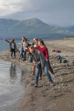 A group of students skipping rocks at a lake with mountains in the background