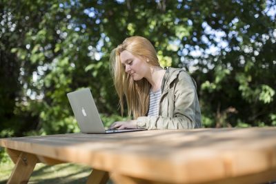 A student sits on a picnic table working on a laptop