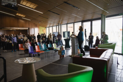 A crowd of people stand around listening to a speaker at the HUBBUB 2025 showcase.