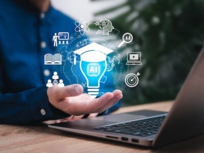 A person's hand open in front a laptop holding an illustration of a lightbulb and other icons related to AI and learning.