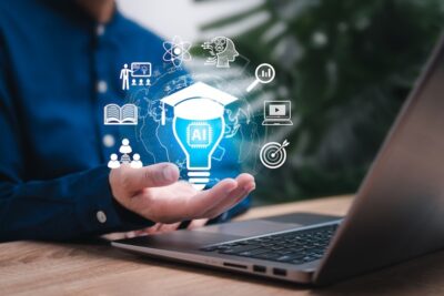 A person's hand open in front a laptop holding an illustration of a lightbulb and other icons related to AI and learning.