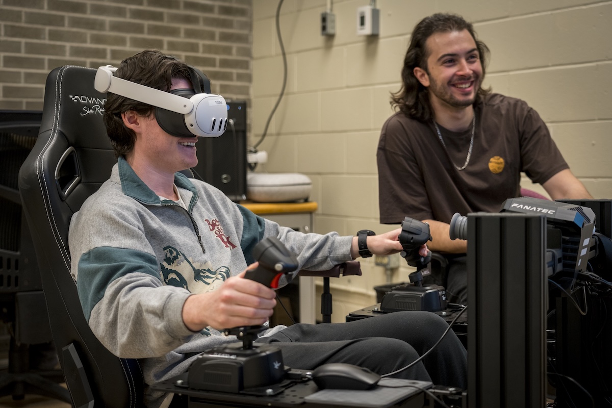 Two students sit smiling at the custom flight simulator acting as pilot and copilot.