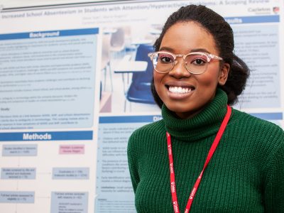 A student smiling in front of their poster presentation at the I-CUREUS and SaPP Showcase