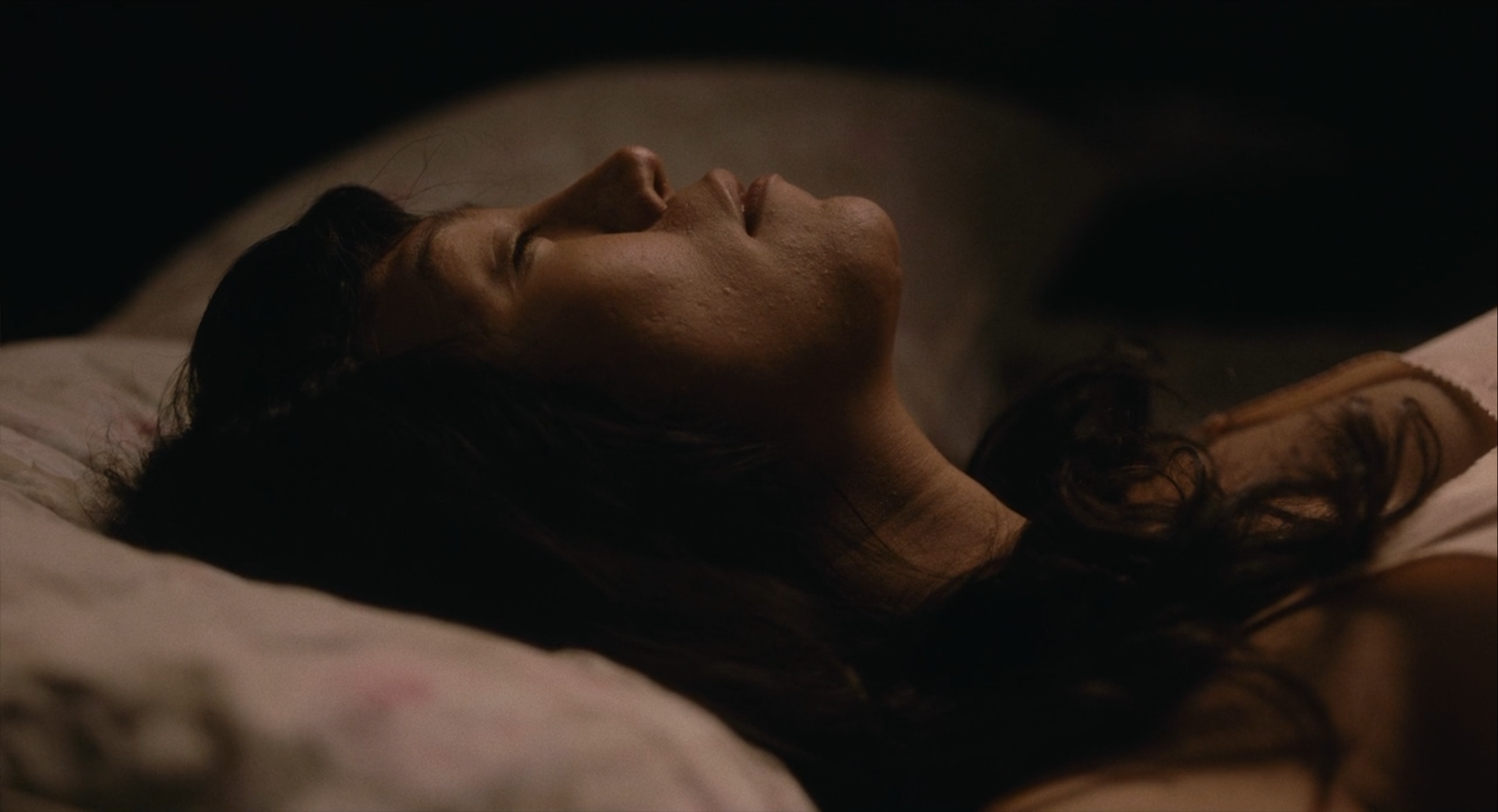 A close-up of the face a Filipina woman lying in bed with her eyes closed, a hint of a smile on her face.