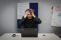 Person looking at their computer in distress, holding their head