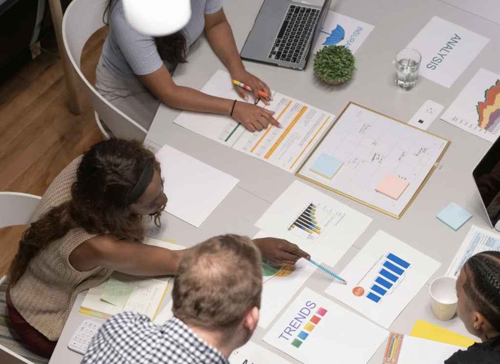 Viewed from above two women of colour and a white man are working on documents for a presentation