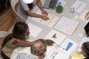 Viewed from above two women of colour and a white man are working on documents for a presentation