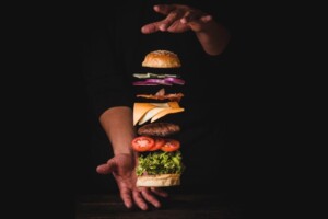 Two hands hover over and under a hamburger separated into sections by ingriedients