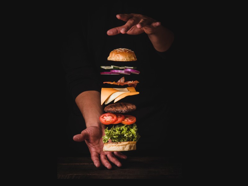Two hands hover over and under a hamburger separated into sections by ingriedients