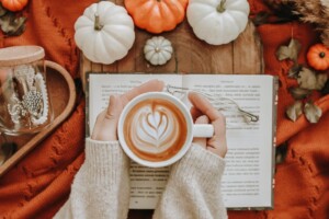 Hands hold a pumpkin latte with Fall colors and items like pumpkins