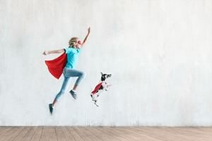 A person pretending to be a super hero leaps in the air with his dog