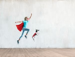 A person pretending to be a super hero leaps in the air with his dog
