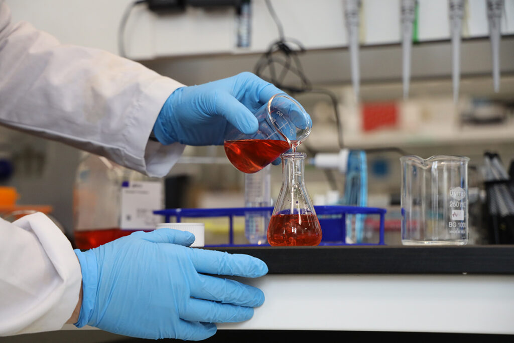 A red chemical being poured into a beaker.