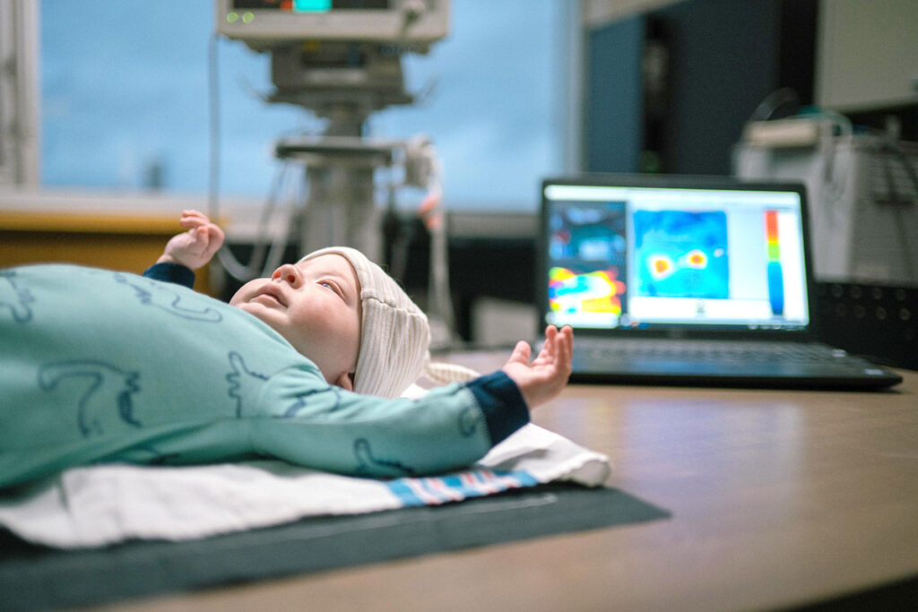 A baby laying on a blanket next to a laptop.