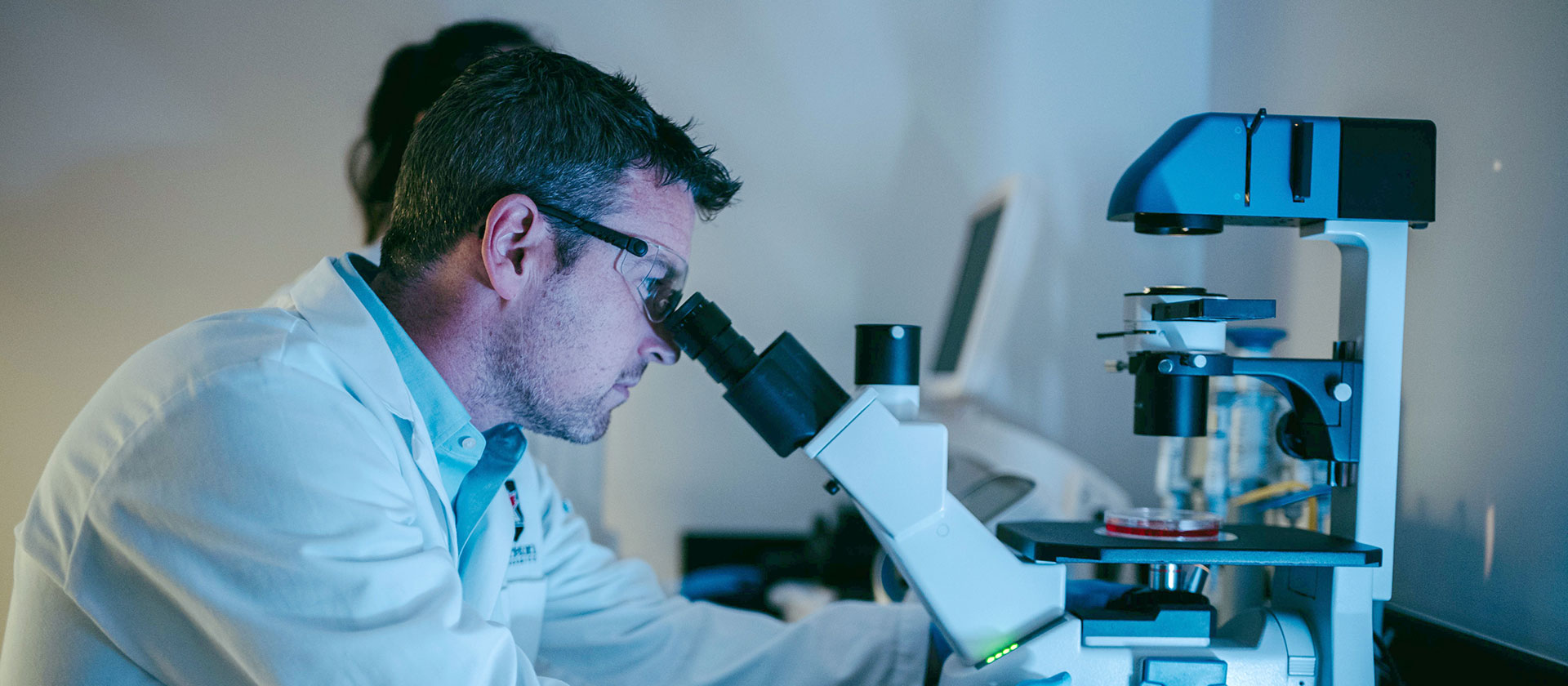 A scientist looking into a microscope inside a lab.