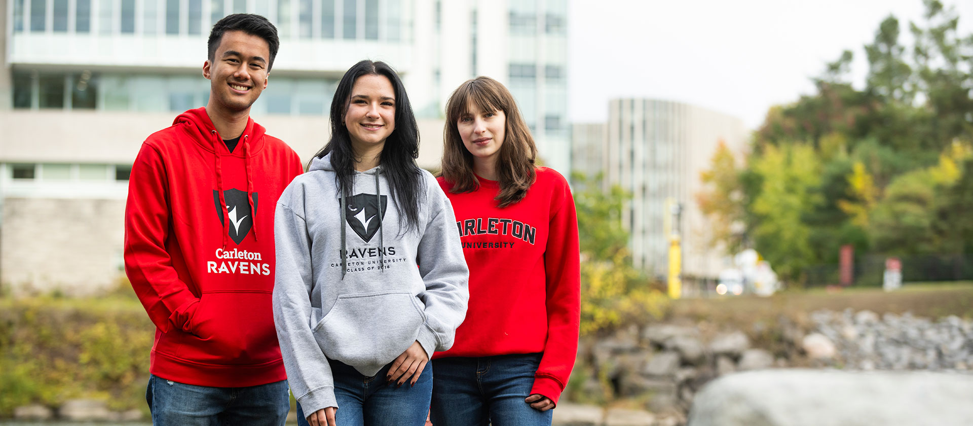 Three students posing for a photo outside, with a building visible in the background.