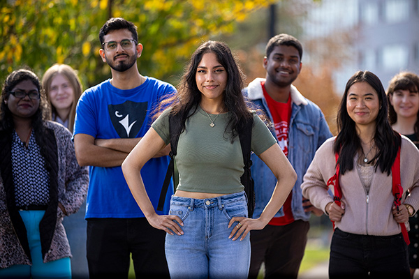 A group of four students smiling and posing at the camera. Standing outside.